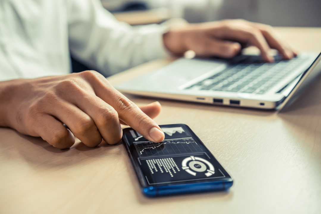 Homem de negócios com celular e computador em mãos analisando dados do controle de prazos.